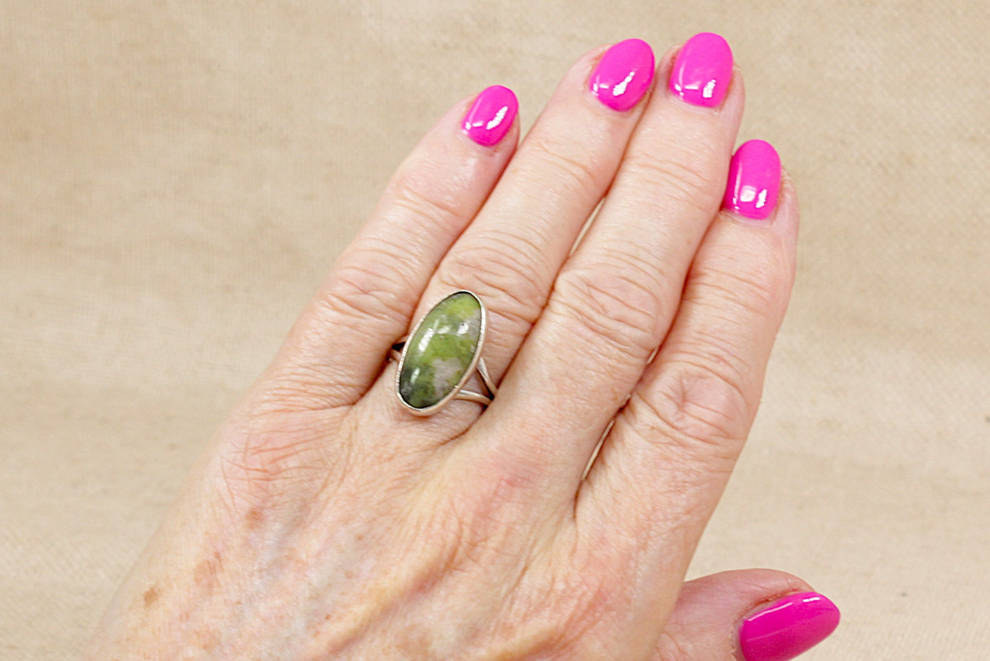 Hand wearing a green agate silver ring with pink nail polish on a beige background