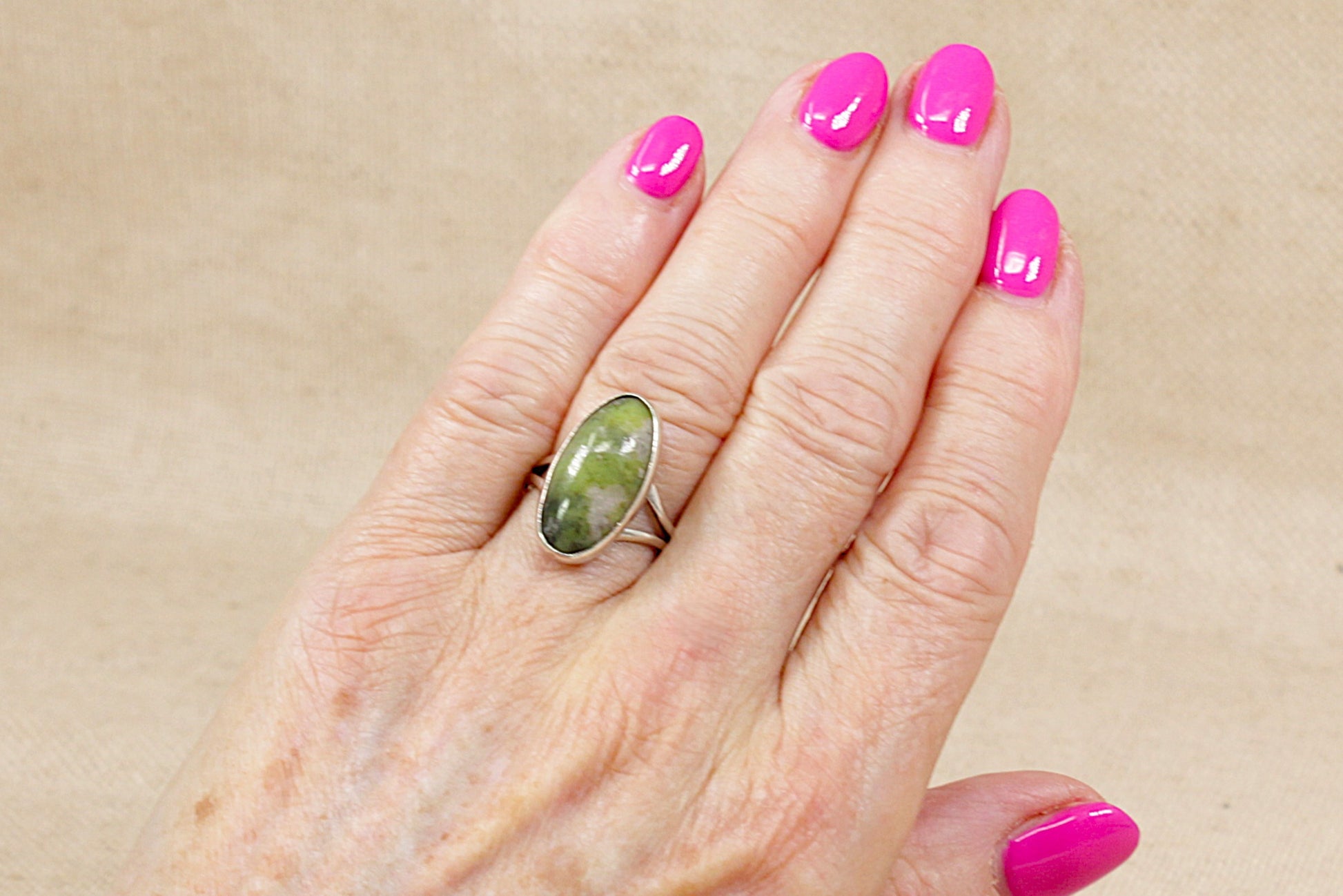 Hand wearing a green agate silver ring with pink nail polish on a beige background