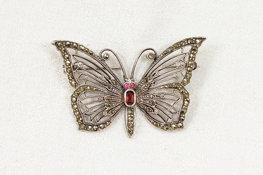 Butterfly-shaped brooch with marcasite garnet and red spinel gemstones on a white background