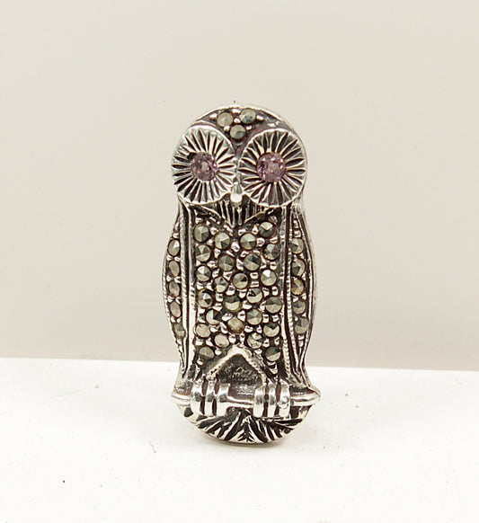 Vintage silver and marcasite owl-shaped brooch with amethyst gemstones eyes on a white background