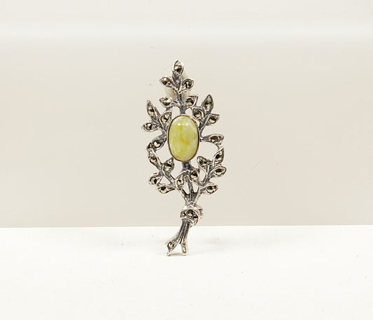 Silver brooch with a green gemstone on a white background