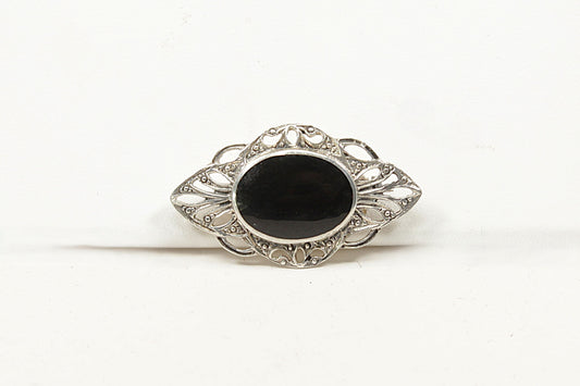 Decorative brooch with a black onyx center and silver intricate design on a white background