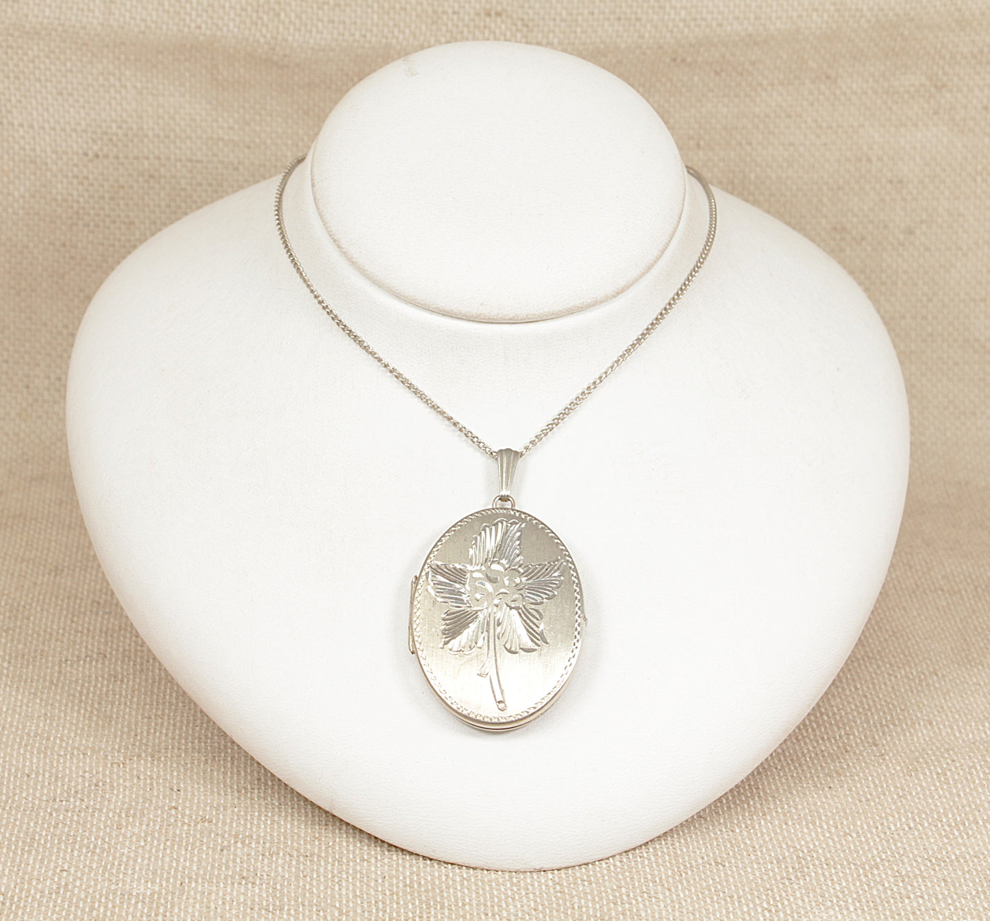 Silver necklace with an oval hinged locket pendant on a white jewelry display