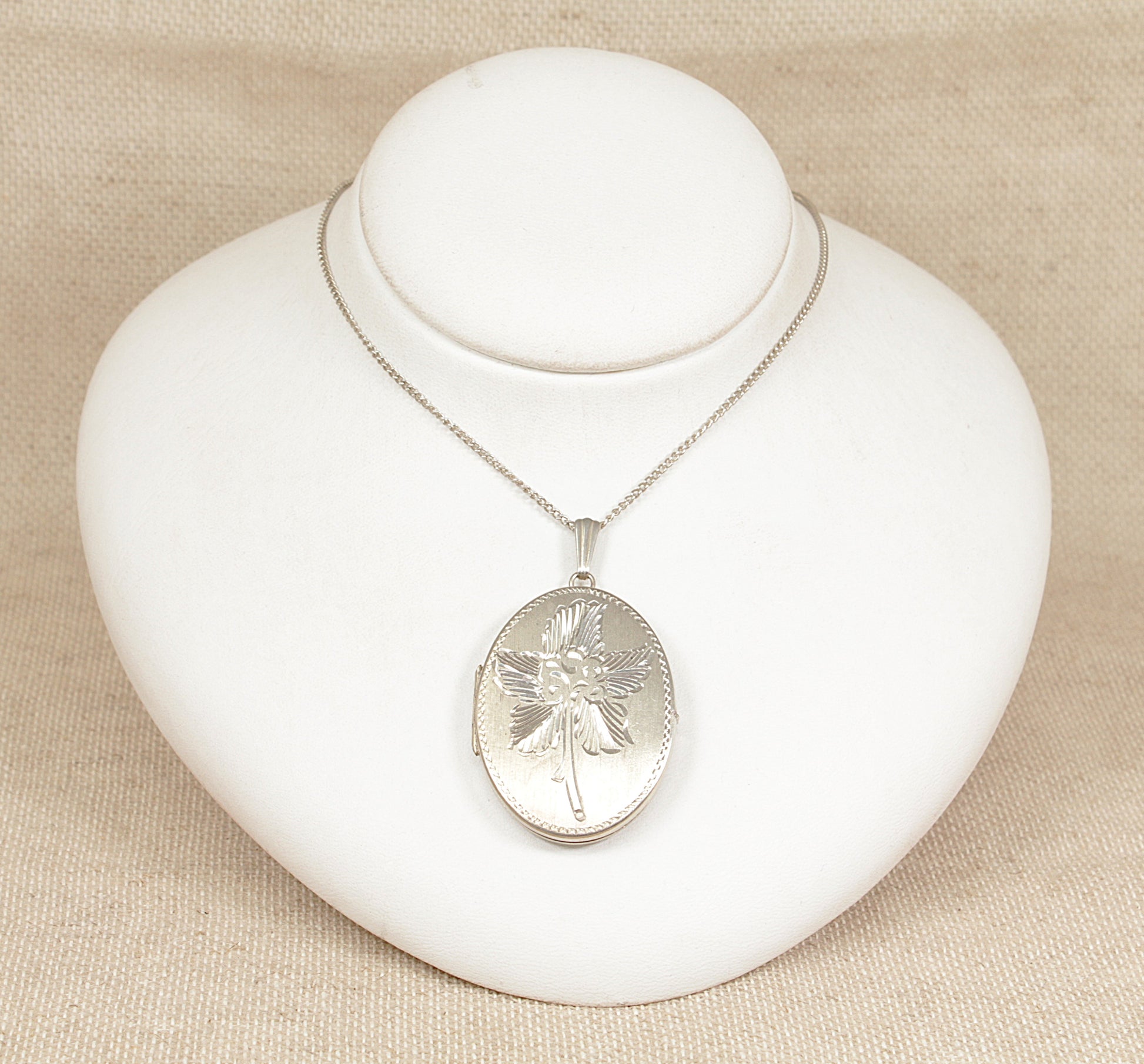 Silver necklace with an oval hinged locket pendant on a white jewelry display