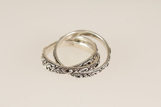Three silver wedding rings with intricate designs on a light beige background