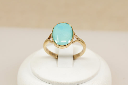 A sleek and elegant 9ct gold ring, showcasing a vibrant oval cabochon Turquoise as its centrepiece. The stone is bezel set in a smooth, polished frame, highlighting its natural beauty and vivid colour. The setting is enhanced by split shoulders, giving the design a clean, contemporary feel with timeless appeal, UK finger size P.